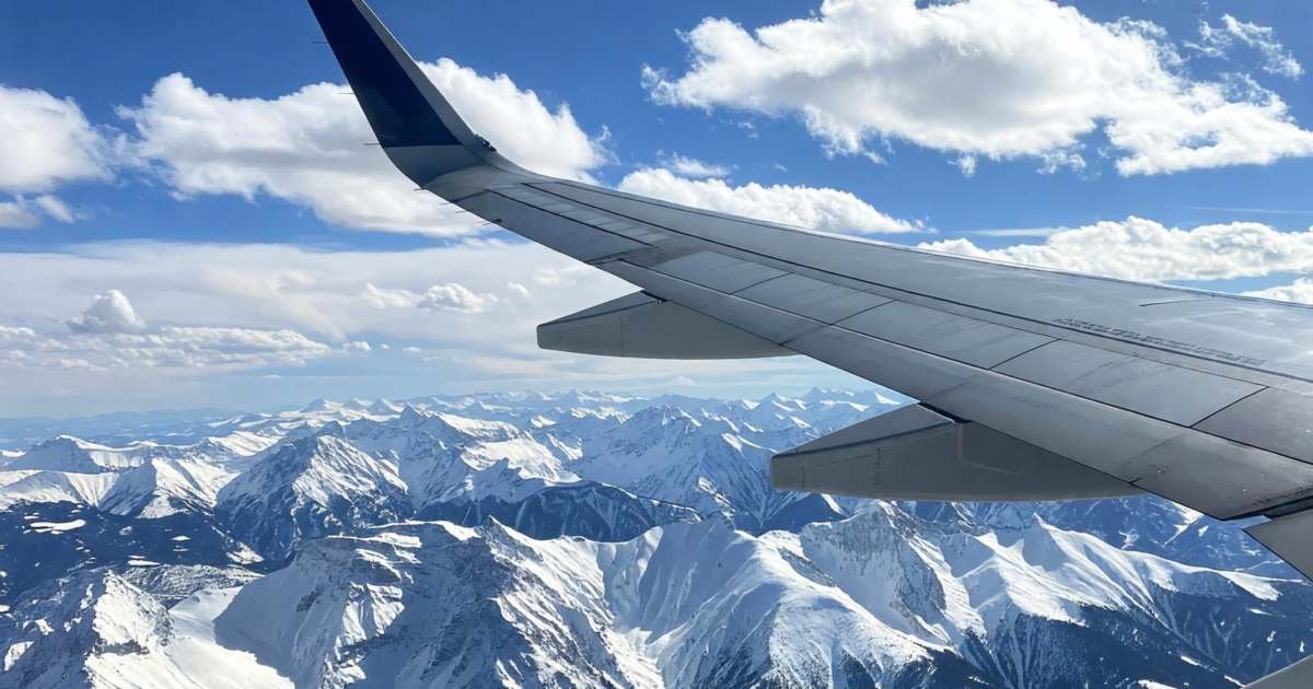 An airplane wing over snow-capped mountains seen from a window seat, illustrating Aeroplan points versus paying cash.