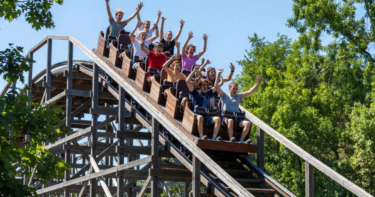 A wooden roller coaster against a summer sky with riders on the first drop, illustrating amusement park season passes for 2027.