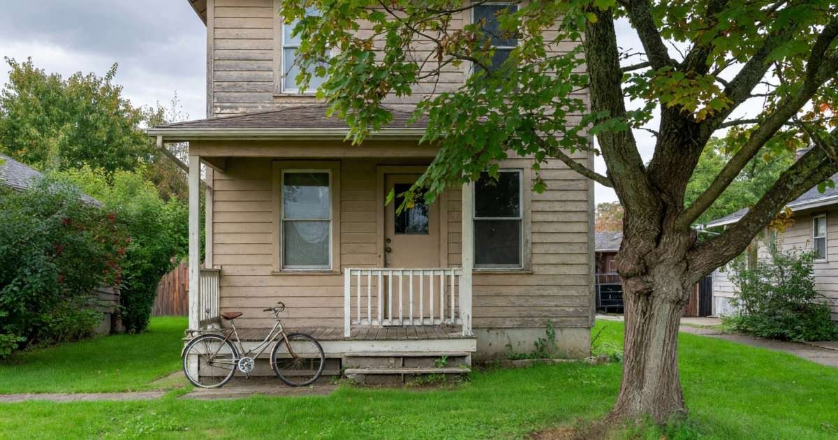 A modest two-storey house with a front porch and a mature maple tree on a quiet residential street, illustrating the B.C. Home Owner Grant and property tax.