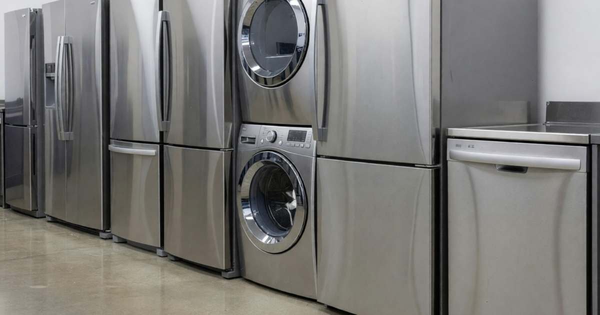 A row of new stainless steel refrigerators, a washer and dryer pair and a dishwasher on an appliance store floor, illustrating when to buy appliances in Canada: Black Friday vs Boxing Day.