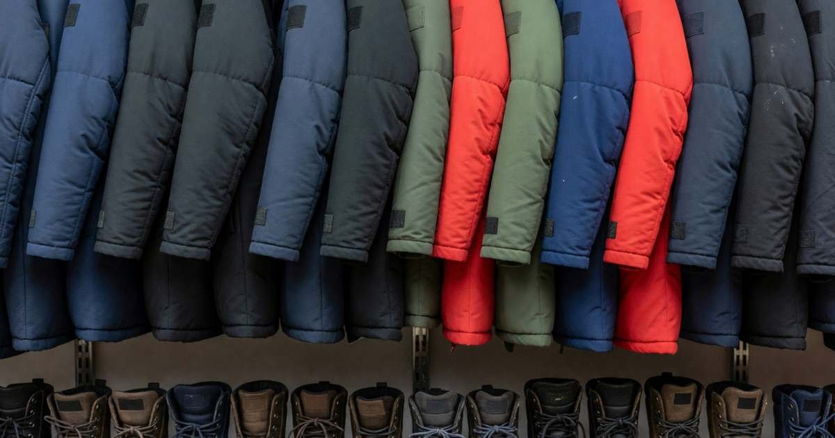 A long rack of heavy winter parkas and a low shelf of winter boots in a quiet clothing store, illustrating Black Friday vs Boxing Day sales on winter coats and boots in Canada.