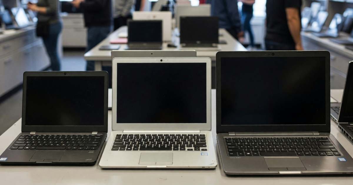 Three laptops of different sizes open side by side on a store display table, screens dark, illustrating buying a laptop in Canada without overpaying.