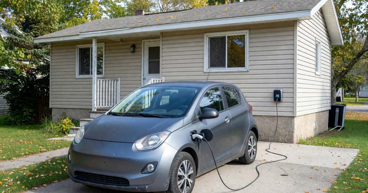 A compact electric car plugged into a charger in a home driveway, illustrating the 2026 EVAP electric vehicle rebate in Canada.