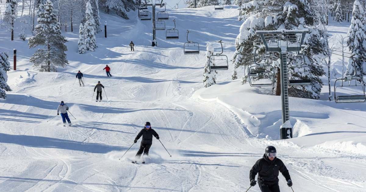 A ski hill with skiers on groomed runs and a chairlift on a sunny winter day, illustrating cheaper lift tickets in Canada.