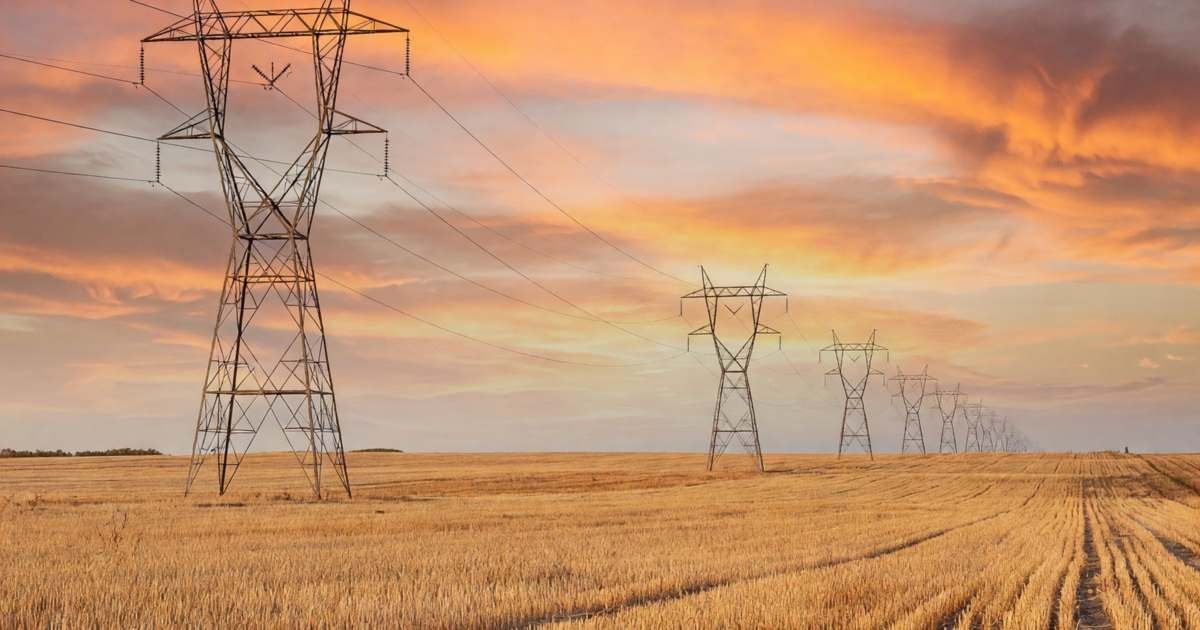 High-voltage transmission towers stretching across a prairie field at sunset, illustrating why electricity bills differ across Canadian provinces.