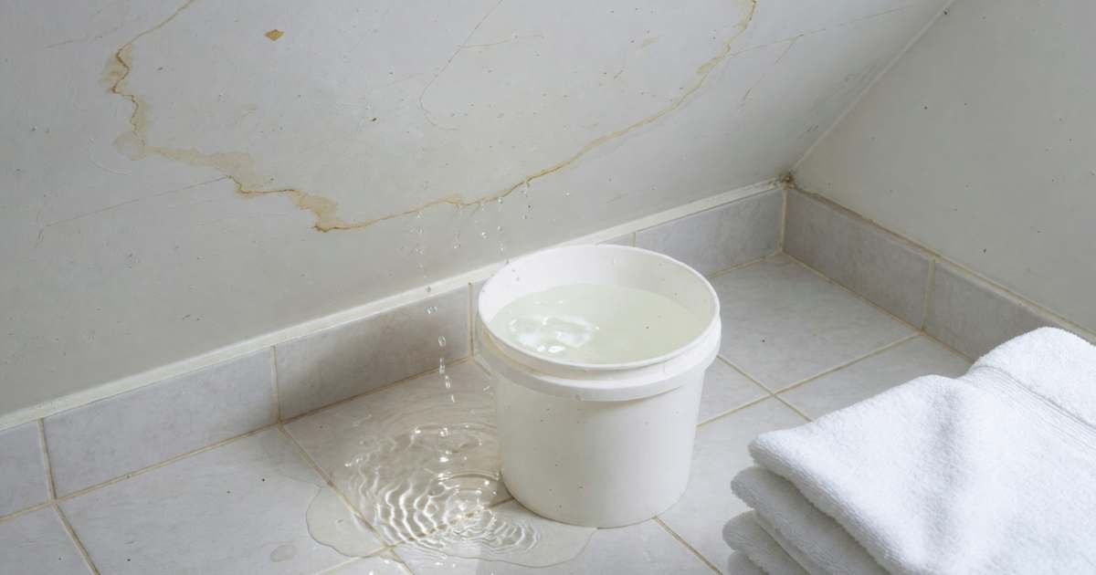 A condo bathroom with water damage on the ceiling and a small puddle on the tile floor below, illustrating condo unit insurance deductibles in Canada.