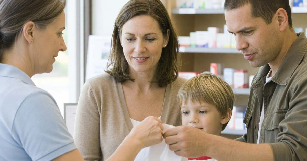 A couple at a pharmacy counter picking up a prescription for their young son, illustrating coordinating two workplace benefit plans in Canada.