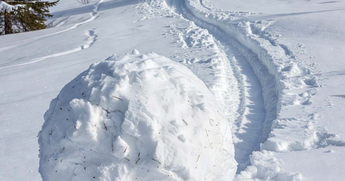 A large snowball rolled up on a snowy hillside, leaving a long track behind it in fresh snow, illustrating the debt snowball vs avalanche methods in Canada.