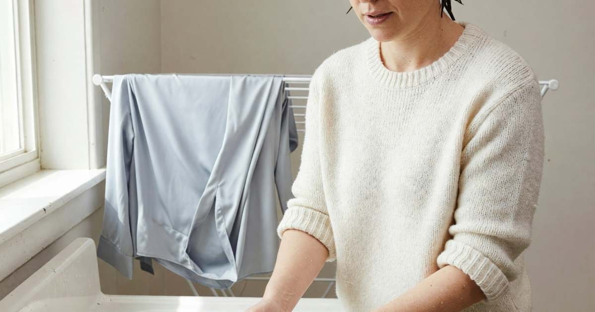 A woman hand-washing a wool sweater in a laundry sink with cool water, illustrating dry cleaning versus safe home care.