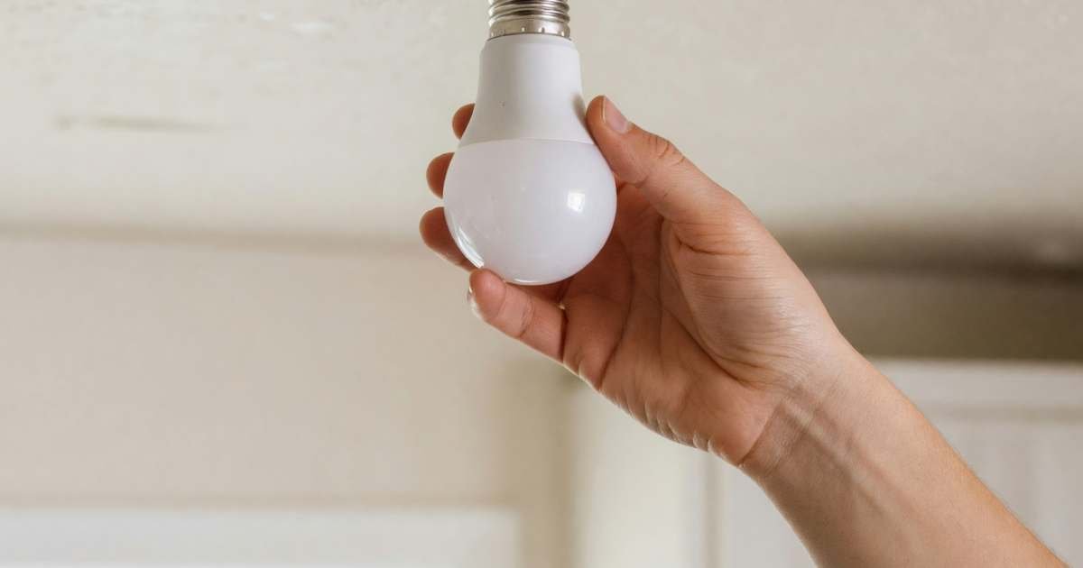 A hand screwing a new LED bulb into a ceiling fixture, illustrating LED lighting upgrades for Canadian homes.