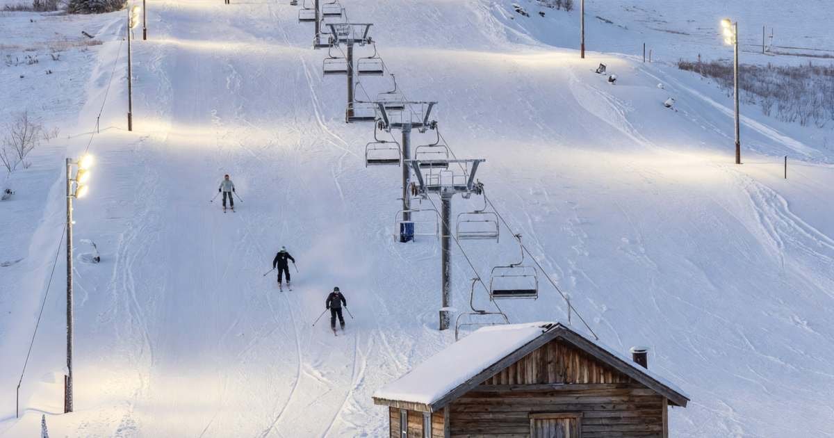 A small local ski hill lit up for night skiing, with floodlit runs and a T-bar lift, illustrating local ski hill season passes in Ontario and Quebec.