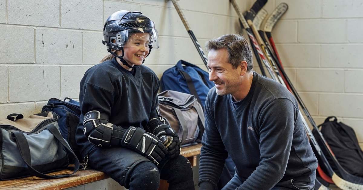 A young girl in full hockey gear sitting on a dressing-room bench while her dad tightens her skates, illustrating the real cost of minor hockey in Canada.