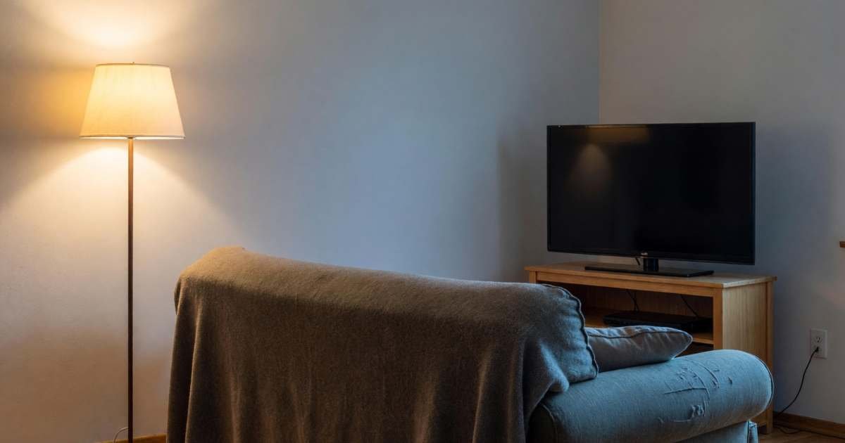 A living room at night with a sofa, a blanket and a TV switched off on a stand, illustrating Netflix Canada plans, ads, pause and cancel.
