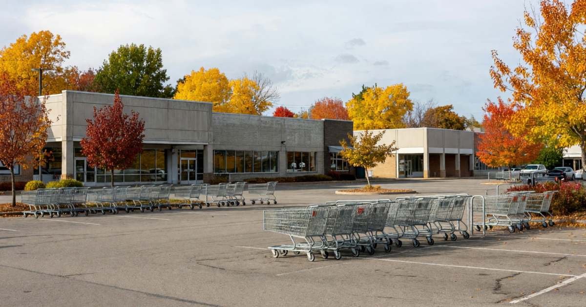 A suburban strip-mall parking lot with several supermarkets side by side, shoppers' carts in the corrals, illustrating rotating between No Frills, FreshCo, Food Basics and Walmart.