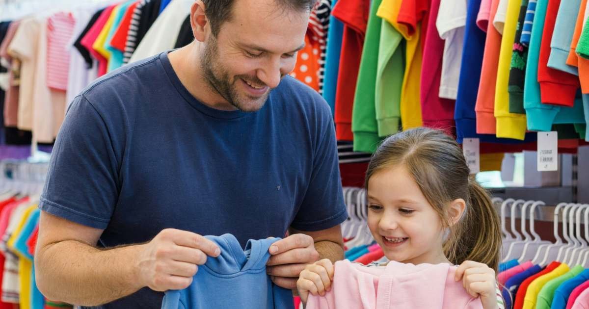 A father and daughter holding up small hoodies in a kids' clothing store, illustrating Old Navy and Gap sale cadence and kids' basics.