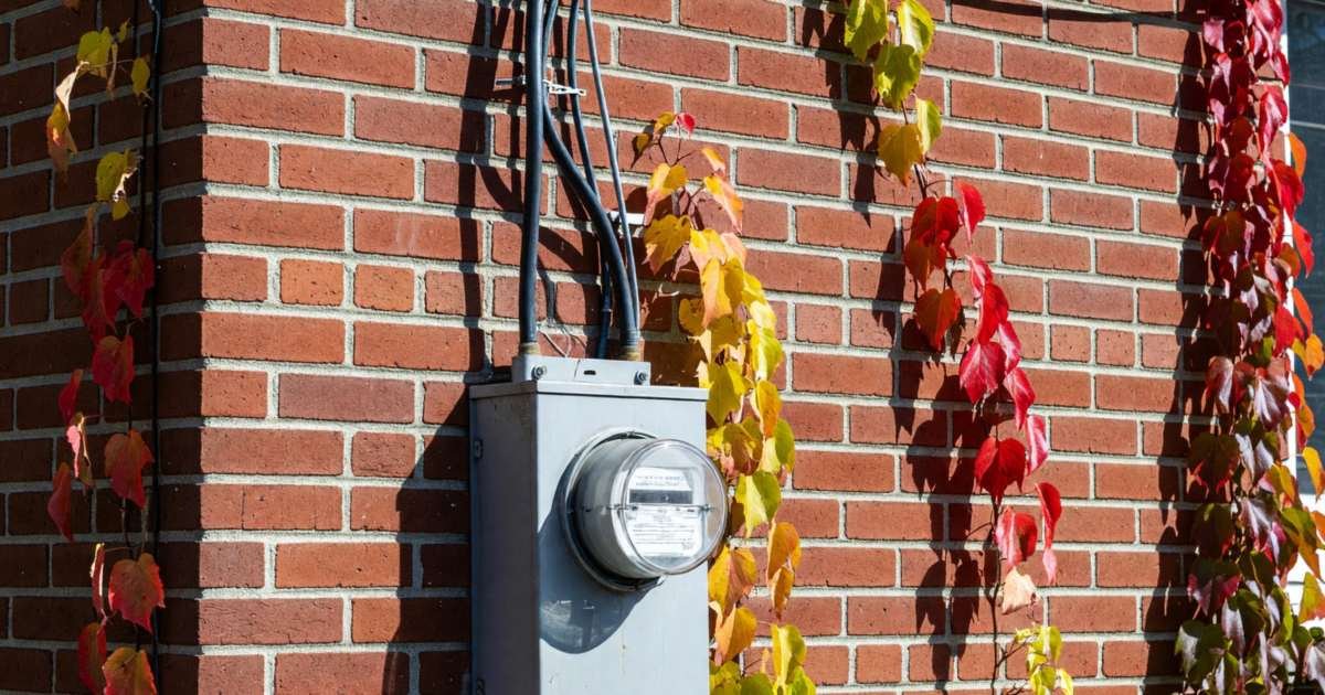 An electricity meter on the brick side wall of a house with wires leading up to the roofline, illustrating the anatomy of an Ontario electricity bill.