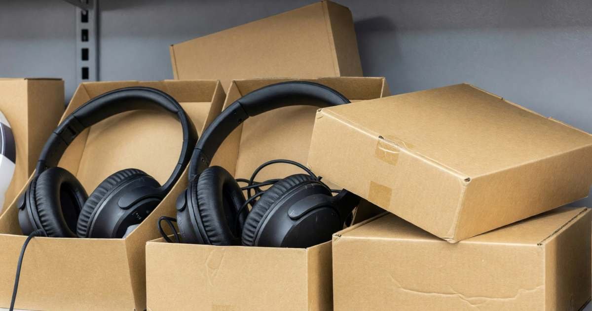 A clearance shelf of open-box headphones, a tablet and a speaker in resealed plain boxes, illustrating open-box and clearance electronics.