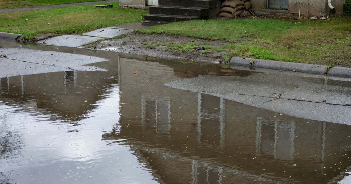 A residential street partly flooded after heavy rain, water up to the front steps of a house, illustrating overland flood insurance in Canada.