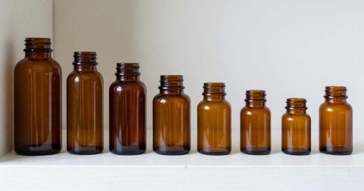 A row of plain amber pill bottles of different sizes on a white shelf, illustrating provincial drug plans across Canada compared.