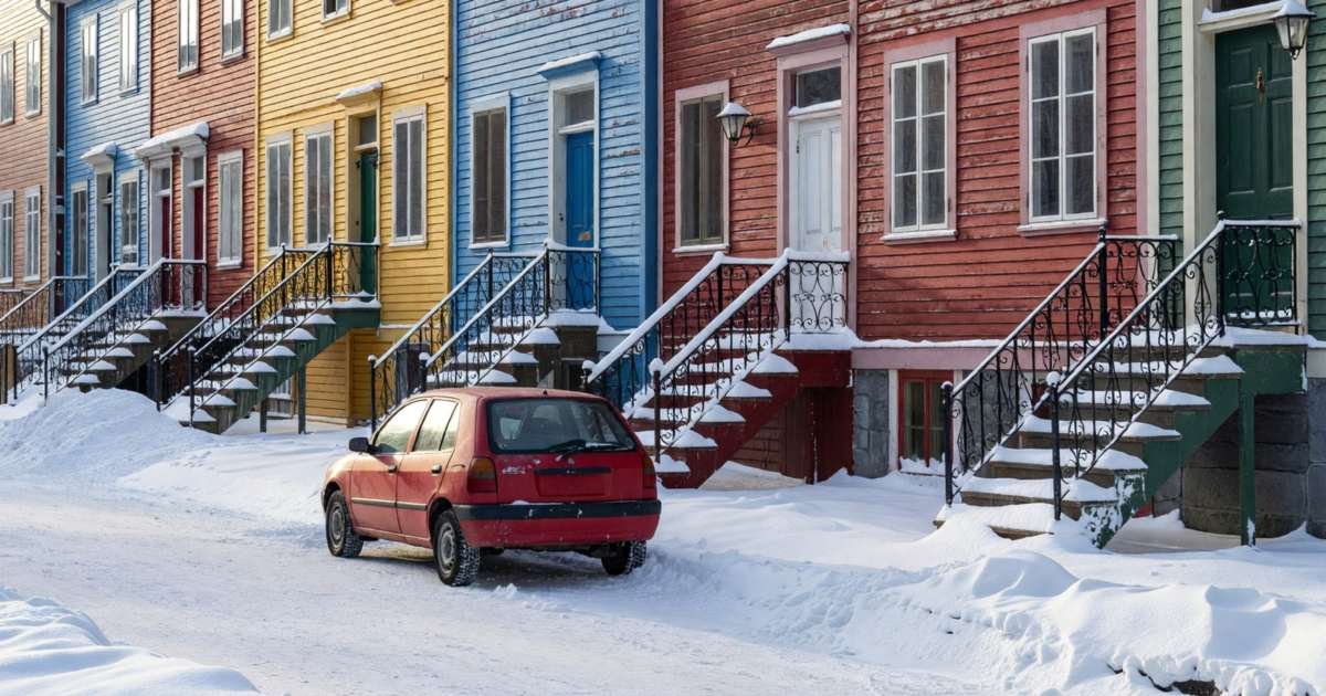 A small car parked on a snowy street lined with colourful row houses, illustrating private damage auto insurance versus SAAQ coverage in Québec.
