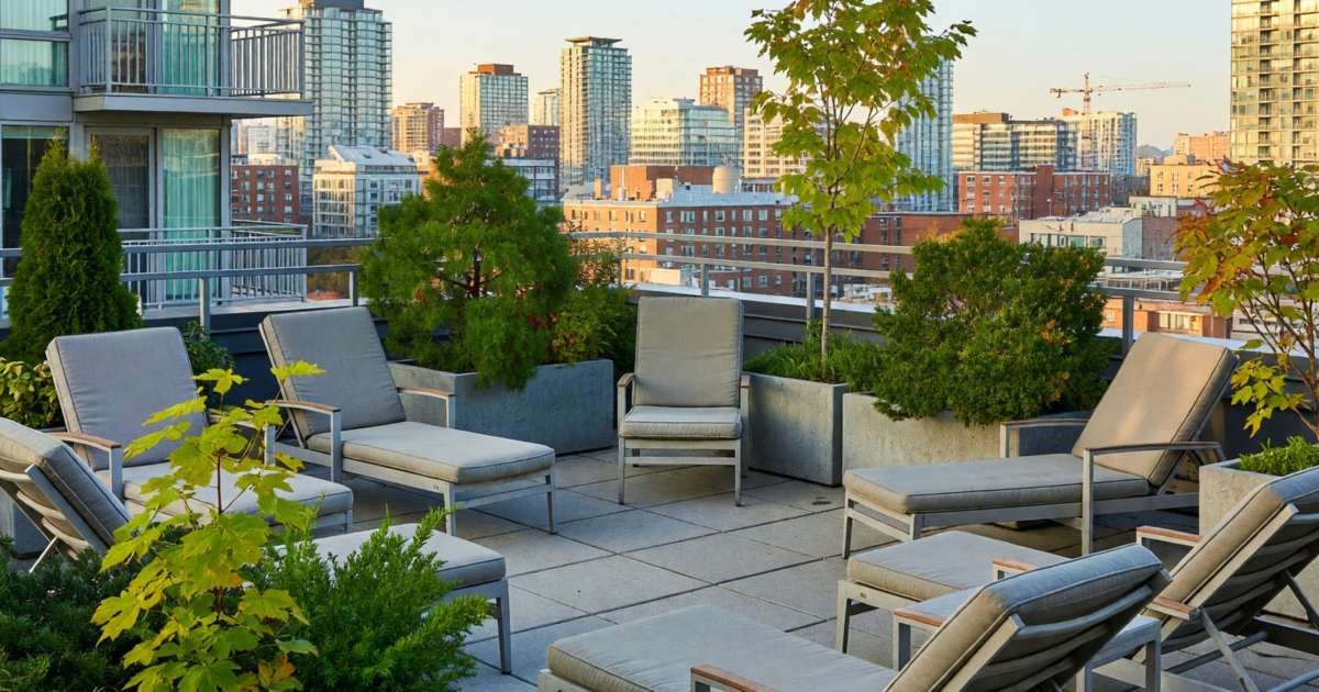 A condo building's shared rooftop terrace with lounge chairs and planters overlooking the city, illustrating renting a condo in Canada, fees and amenities.
