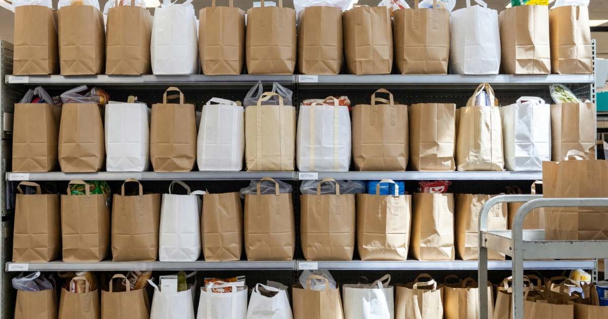 A row of filled grocery bags waiting on shelves in a supermarket online-order pickup area, illustrating saving at Loblaw online and when in-store still wins.