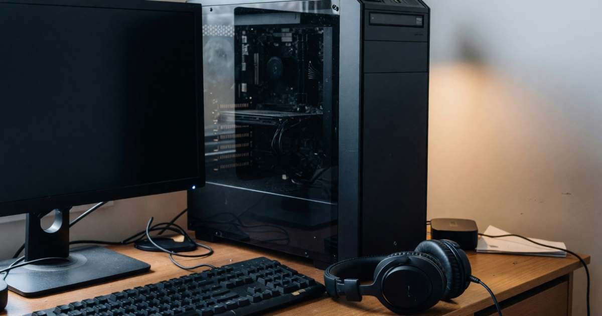 A gaming PC setup on a desk with a mechanical keyboard and a headset, illustrating PC game sales and cheaper PC gaming.