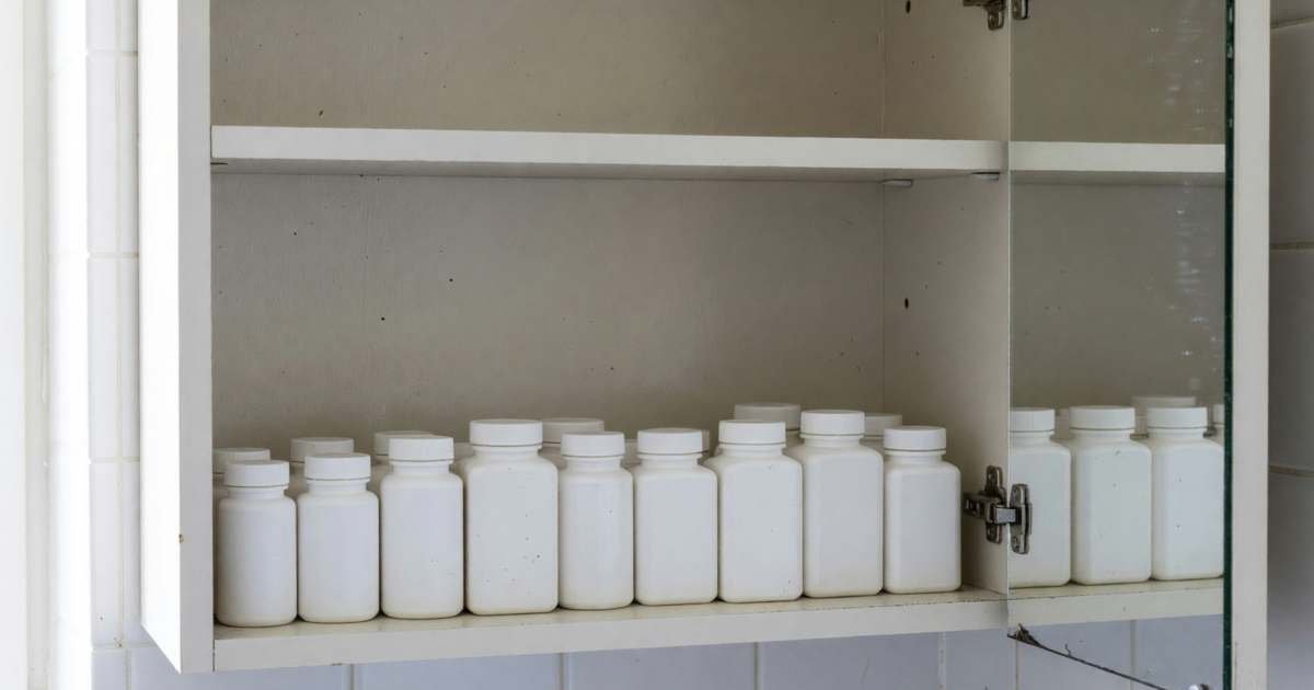 A medicine cabinet with plain white bottles of pain relievers and allergy tablets lined up, illustrating store-brand over-the-counter medicine in Canada.