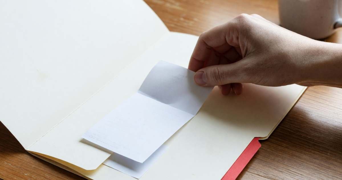 A hand placing a plain receipt into a folder labelled only with a coloured tab, illustrating the student loan interest tax credit.