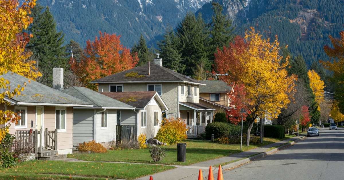 A residential street of houses with mountains in the background and fibre utility work on the boulevard, illustrating Telus PureFibre versus Rogers/Shaw cable in Alberta and BC.