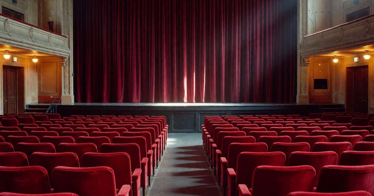 A theatre auditorium with velvet seats and the stage curtain closed, illustrating theatre subscription versus single tickets.