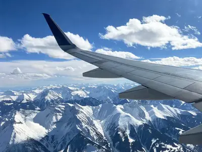 An airplane wing over snow-capped mountains seen from a window seat.