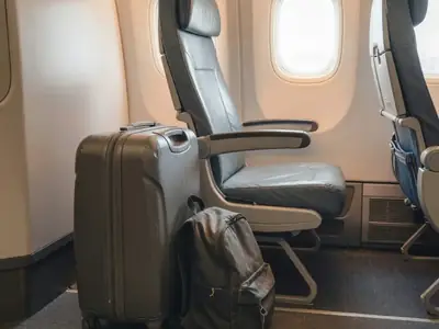 A carry-on suitcase and a small backpack next to an airplane seat in the aisle.