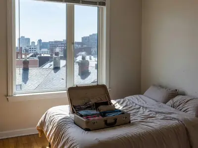 A cosy rental apartment bedroom with a city view, a suitcase open on the bed.