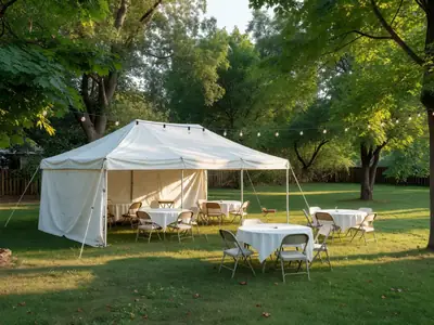 A white rented tent set up in a large backyard with round tables, chairs and string lights.