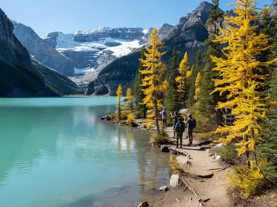 Turquoise Lake Louise with mountains and a few hikers on the shoreline trail.