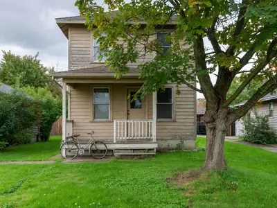 A modest two-storey house with a front porch and a mature maple tree on a quiet residential street.