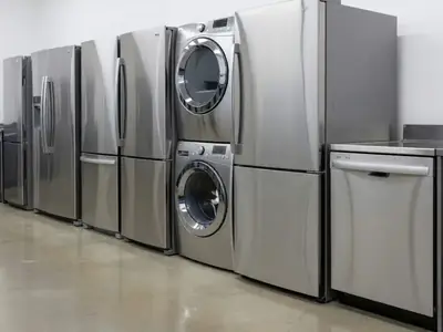 A row of new stainless steel refrigerators, a washer and dryer pair and a dishwasher on an appliance store floor.
