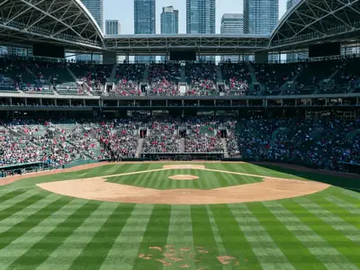 A baseball stadium with an open roof on a sunny afternoon, fans in the upper deck.