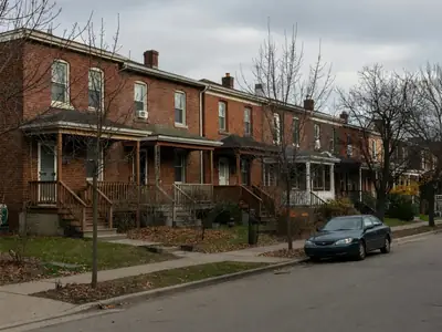 A row of narrow brick semi-detached houses with small front gardens on a quiet street.