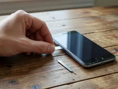 A hand sliding a tiny SIM card tray into the side of a slightly worn smartphone.