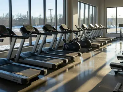 A row of empty treadmills and bikes in a large fitness club at early morning.