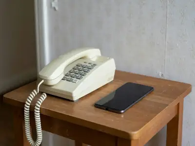 An old corded landline telephone on a hallway table beside a modern smartphone.