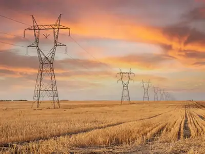 High-voltage transmission towers stretching across a prairie field at sunset.