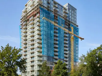 A condo tower with scaffolding and construction netting on part of its facade and a crane nearby.