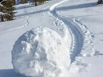 A large snowball rolled up on a snowy hillside, leaving a long track behind it in fresh snow.