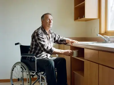 A man using a wheelchair working in his kitchen, reaching for a mug on a lowered counter.