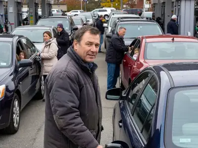 A man filling up his car at a busy warehouse-club gas bar with long queues of cars.