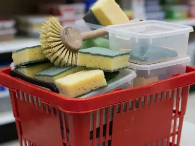 A shopping basket filled with cleaning supplies, sponges, a dish brush and storage bins.