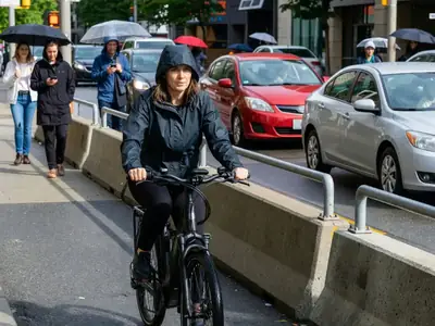 A woman in a rain jacket riding an e-bike along a protected bike lane.